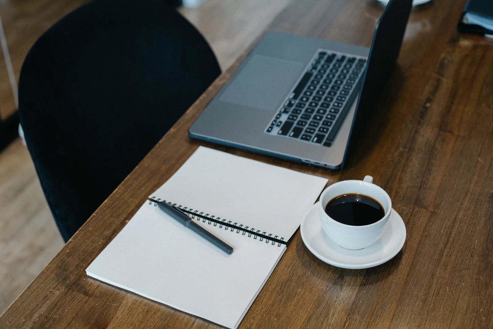 Laptop, Notizblock und eine Kaffeetasse auf einem hellen Schreibtisch von oben fotografiert.