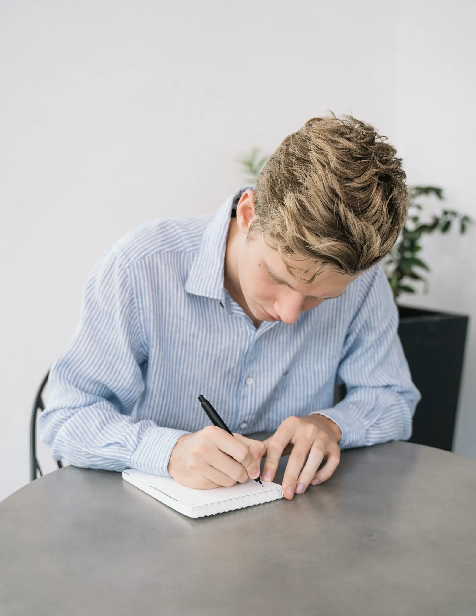 Junger Mann schreibt zuhause am Tisch in ein Notizbuch.