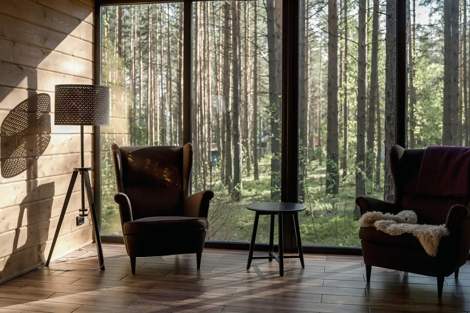 Zwei leere Sessel stehen an einem großen Fenster mit Blick in einen Wald.